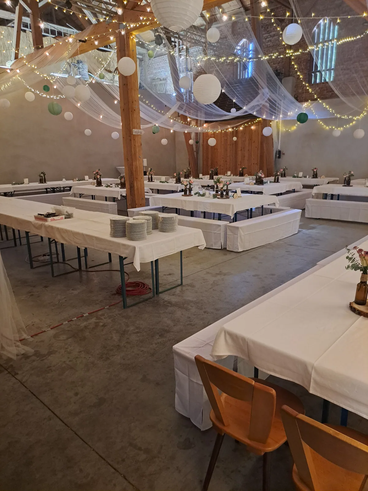 Weiß eingedeckte Biertischgarnituren im Stadl unter Lichterketten